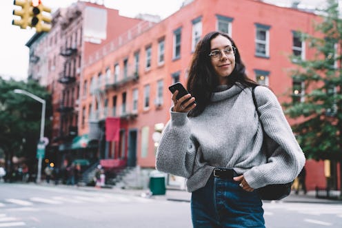 Beautiful slim smiling woman in glasses with black bag wearing denim and sweater looking away and br...