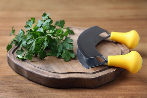 Cutting board with parsley and mezzaluna knife on wooden table