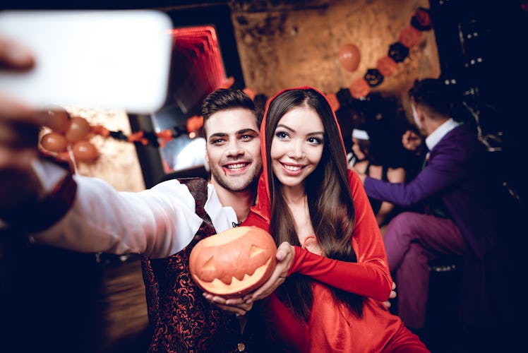 Halloween party. A guy in a vampire costume and a girl in a red dress with a hood making selfie with...