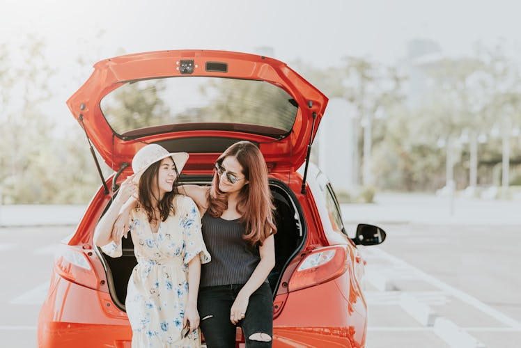Happy Asian girl best friends traveler laugh and smile together while sitting in car trunk during va...