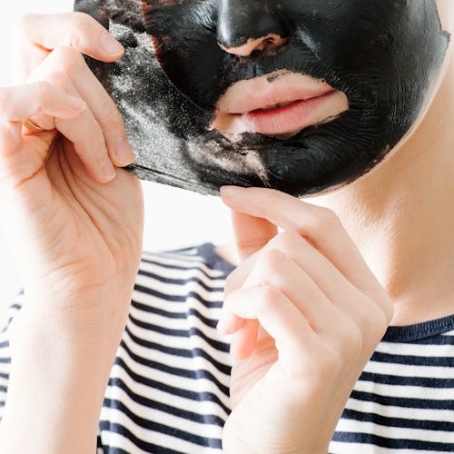 Young woman in striped half sleeve removing bamboo charcoal peel off facial mask at home. Over white...