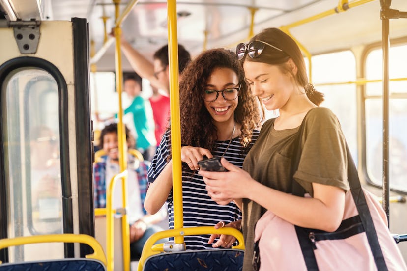 Two friends laughing and watching phone while waiting for bus to depart.