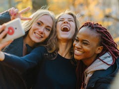 Three Pretty woman making selfie in autumn park. Cute girls with different colored skin. Female maki...