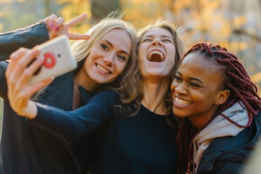 Three Pretty woman making selfie in autumn park. Cute girls with different colored skin. Female maki...
