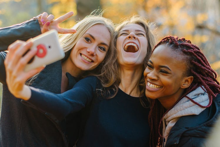 Three Pretty woman making selfie in autumn park. Cute girls with different colored skin. Female maki...