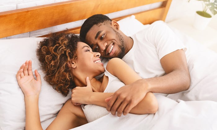 Happy morning together. Millennial african-american couple smiling to each other in bed, free space