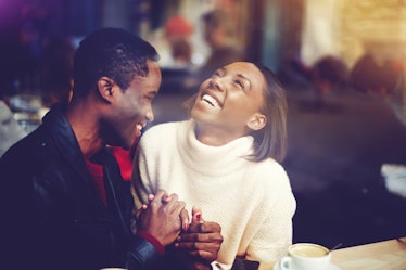Young happy man and woman laughing together while sitting in modern restaurant during coffee break, ...