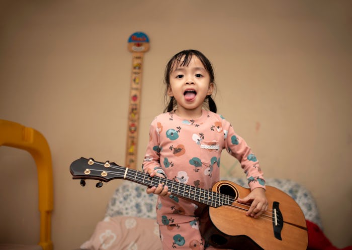 Little girl rock star in pajamas with Ukulele.and she making a tongue out in the living room