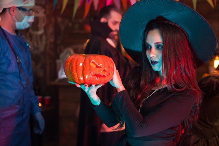 Portrait of beautiful woman dressed up like a witch doing dark magic on a pumpkin for halloween. Dra...