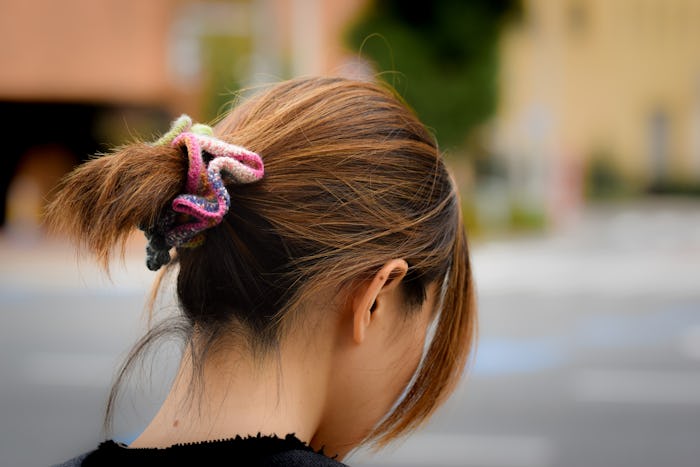 A brunette Japanses woman looks down and away, wearing a colourful scrunchie in her hair.