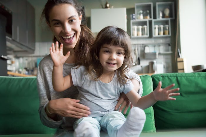 Portrait of happy excited young mother and kid girl waving hands looking at camera, smiling mom with...