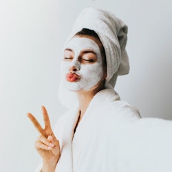 woman has fun with a facial mask.Self portrait of charming, stylish, pretty, model after bath wrappe...