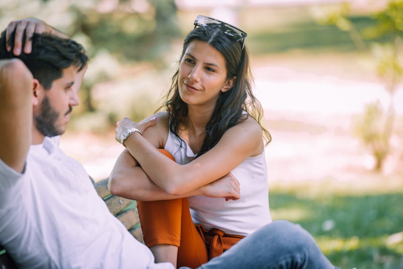 Friends or couple laughing and taking a conversation sitting on a bench in a park