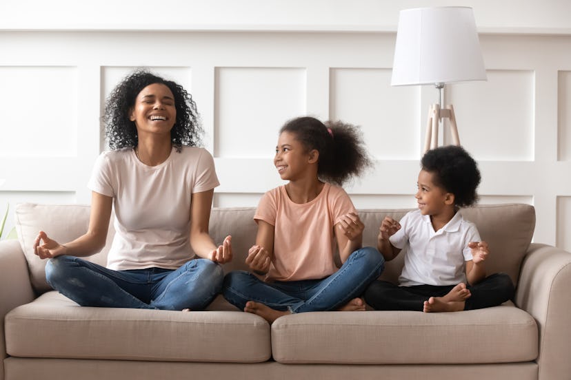 Happy laughing single black mom meditating with two kids at home, healthy african family mother teac...