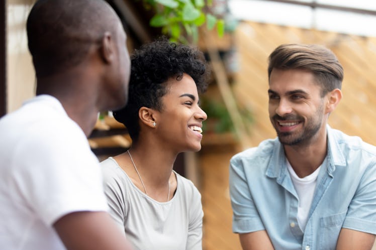 Three millennial multi-ethnic friends spending weekend together sitting in cafe or restaurant cozy s...