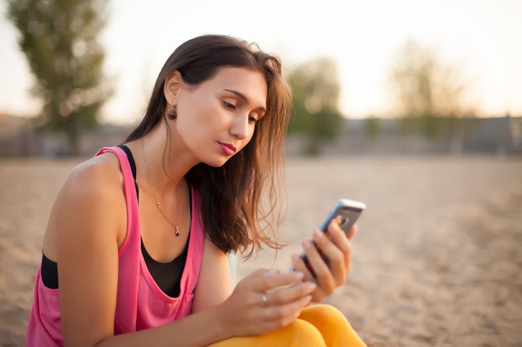 woman texting on smart phone on the beach during sunset