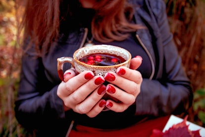 Autumn. Girl with bright red nails siting in autumn park and holding cup of tea with dogrose berries...
