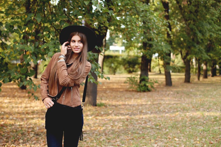 Street fashion concept - closeup portrait of a pretty girl. Wearing hat and suede jacket holding bag...