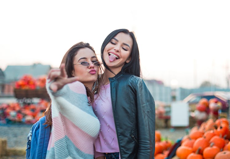 Fashionable beautiful young girlfriends together at the autumn pumpkin patch background. Having fun ...