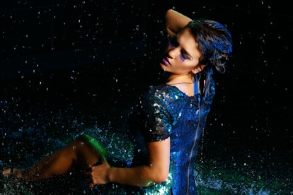 Young sexy woman sitting on wet floor with water drops. Gren light effect. Seductive girl dressed in...