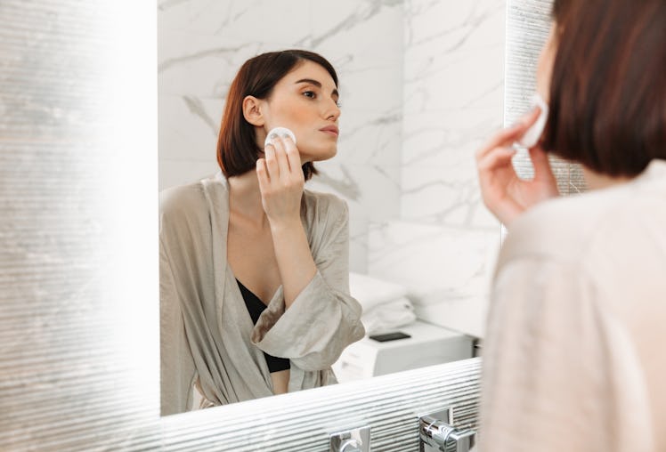 Beauty portrait of brunette woman with soft healthy skin removing makeup with cotton pad in hotel ba...