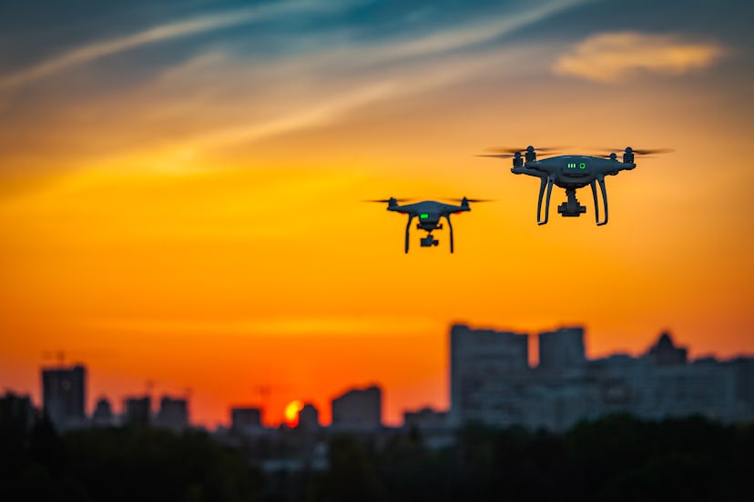 Two drone quad copters with high resolution digital camera flying aerial over spectacular sunset ora...