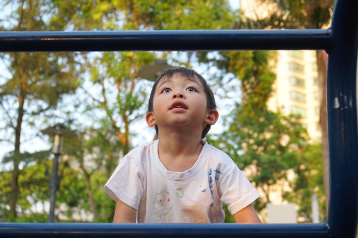 Cute and happy big eyes black hair Asian boy in dirty white T-shirt playing joyfully in the park pla...