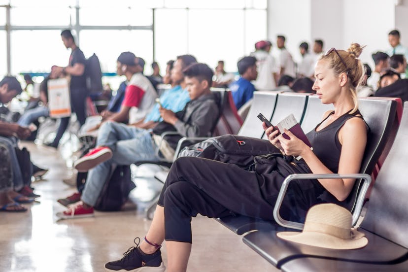 Casual sporty young blond female traveler using her cell phone while waiting to board a plane at the...