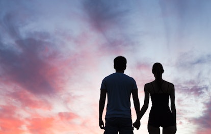 Silhouette of young couple holding hands looking at the sunset