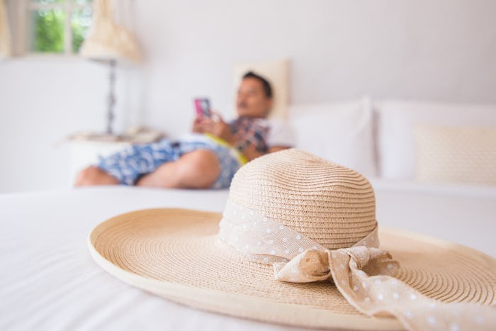 hat are on the white bed in the hotel and a man use mobile phone back.