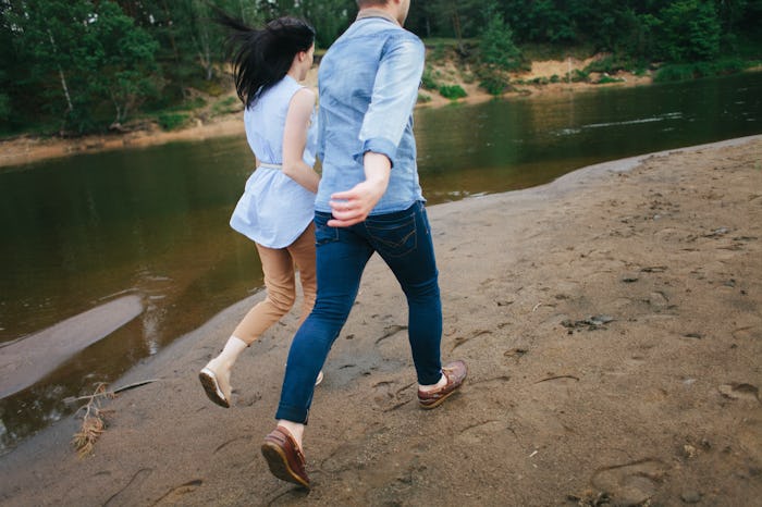 A couple in love runs along the shore. Two people running with their backs to the camera. The girl a...