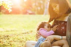 Hispanic mexican mother breastfeeding a dark-skinned mixed race toddler three year old daughter sitt...