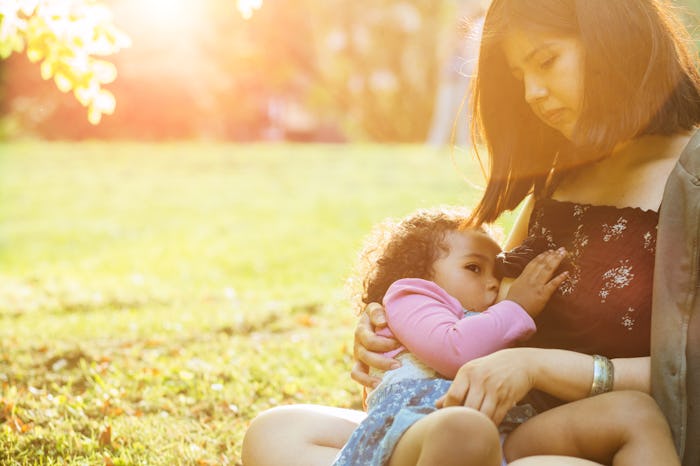 Hispanic mexican mother breastfeeding a dark-skinned mixed race toddler three year old daughter sitt...
