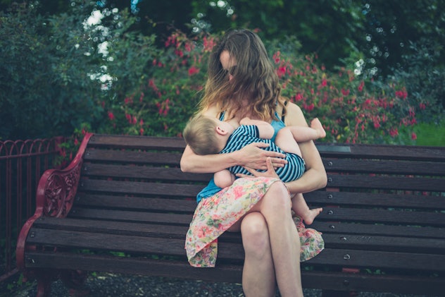 A young mother is breastfeeding her baby on a park bench