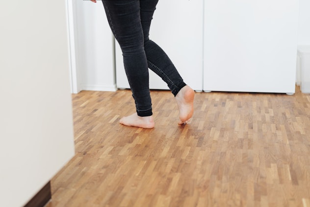 Barefoot young woman walking across a wooden floor turning to pass through a door in a low angle vie...