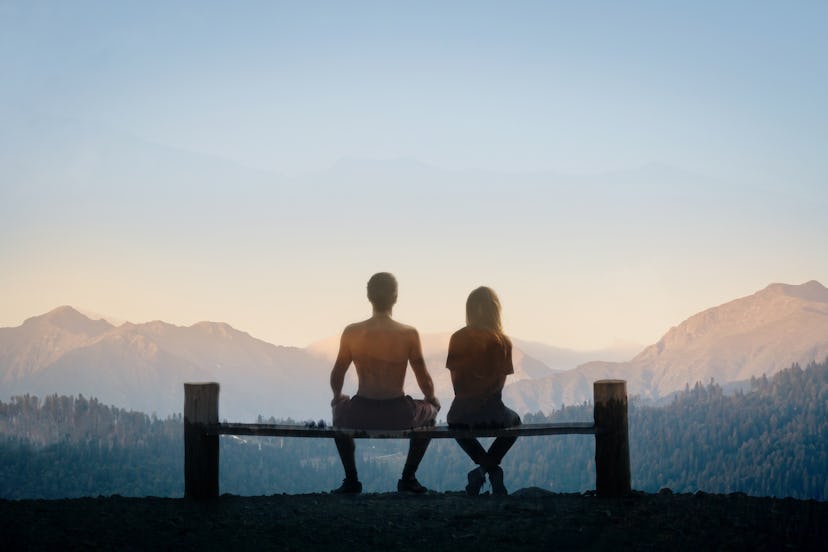 couple - a man and a woman sitting on a bench back to the camera and looking at the mountains. multi...