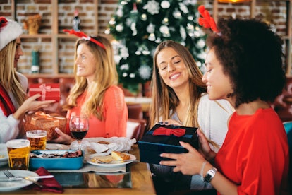 Friends giving gifts to each other while sitting at table. In background Christmas tree. Christmas h...