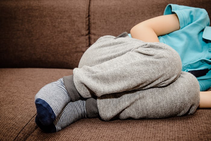A little boy, child is lying on the bed and holding his belly. Baby's medication and health concept....