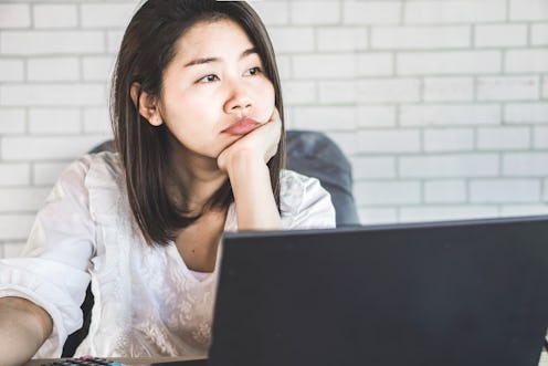 unmotivated Asian female worker sitting at desk bored to work thinking of 
quitting job