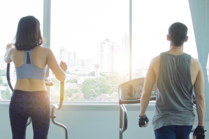 Back of a couple is exercising in fitness center in the morning with the warm light and cityview out...