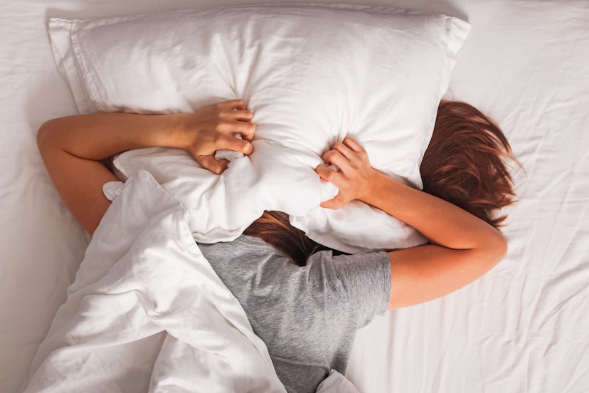Woman lying in bed and covering her head with pillow. Struggling from insomnia, noise or early morni...