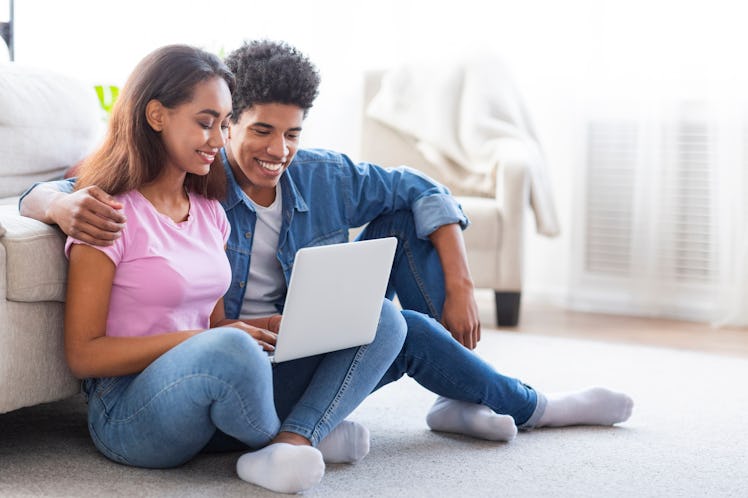 Black teen boy and girl using laptop, browsing on internet or watching movie online, sitting on floo...