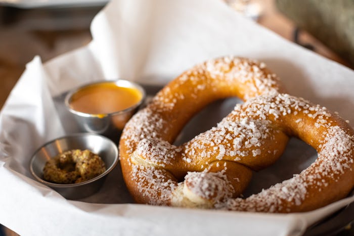 Close up on a salted soft pretzel in a parchment paper lined basket, with mustard and cheese dipping...