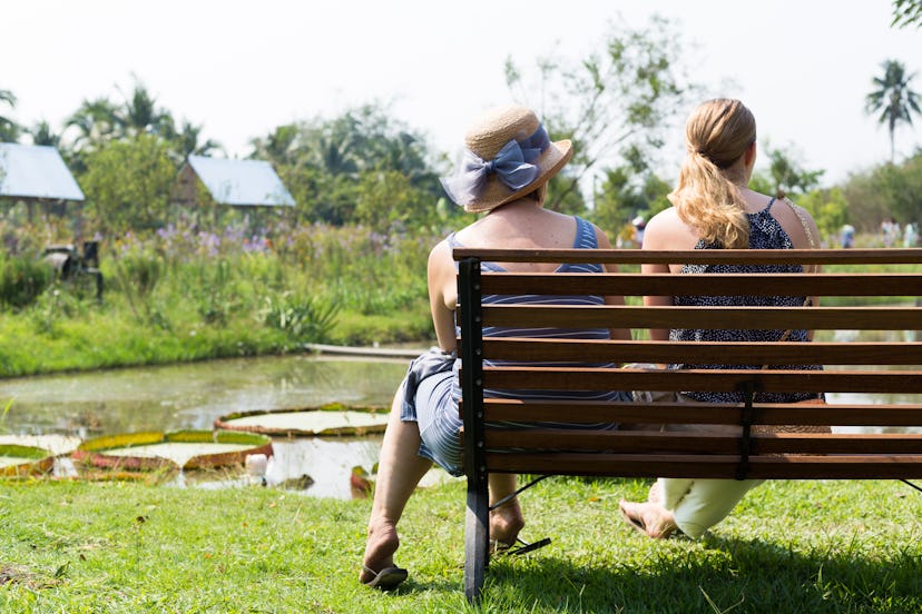 Back of couple women's sitting together on a bench in a park.