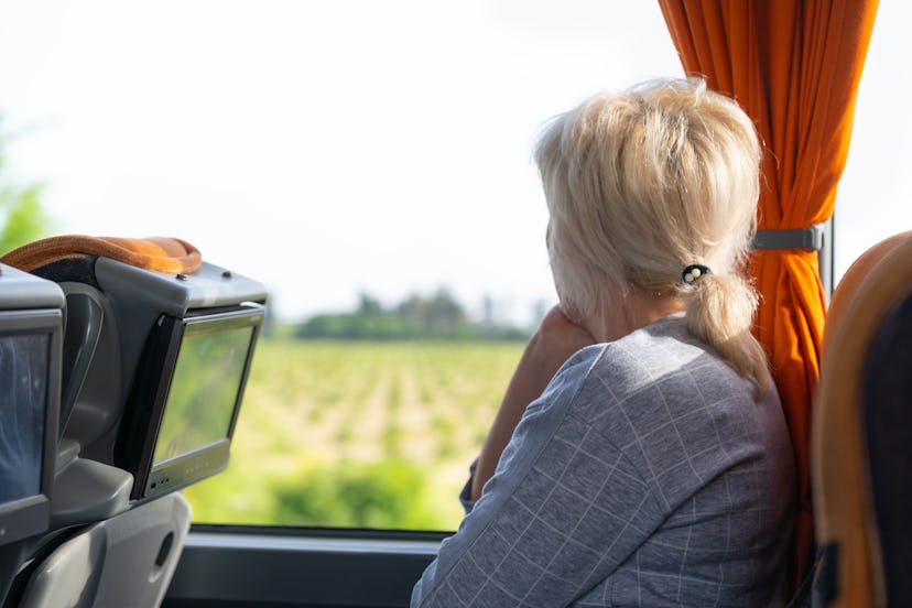 Woman looking out of the window of a coach or train watching the passing countryside as she travels ...