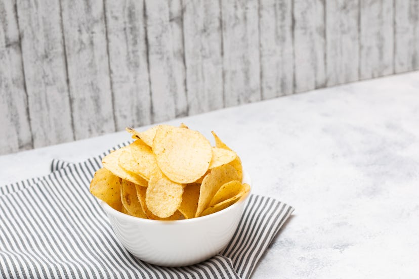 Potato chips in a bowl with white wooden vintage backdrop