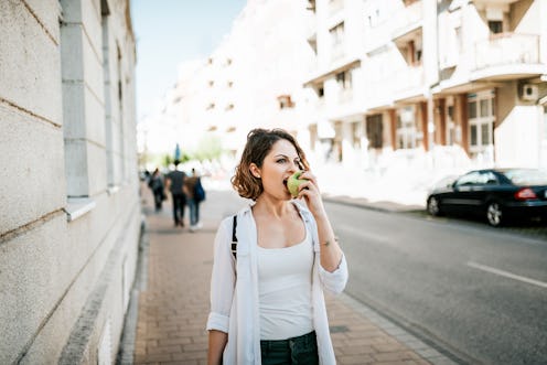 Attractive young woman walking on street and eating an apple.