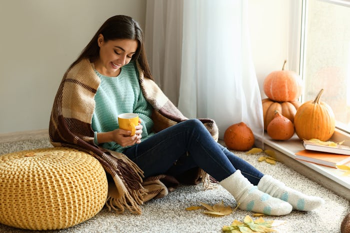 Woman drinking tea while resting at home on autumn day