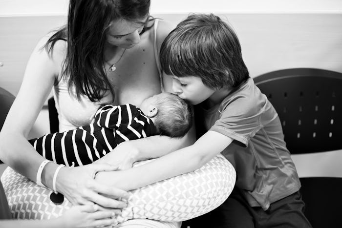 Happy mother of three children, after birth in hospital, children visiting their new baby brother da...