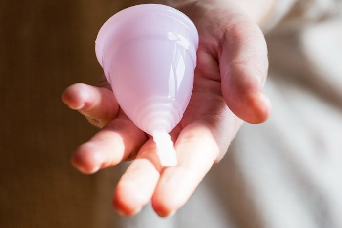 Pink menstrual cup hold in woman's hands.